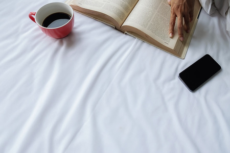 Beautiful asian female sitting on the bed with a cup of coffee and reading a book. Morning with a book and cup of coffee. Relaxing concept. Retro filter effect,soft focus,selective focus.の写真素材