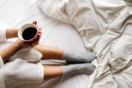 Beautiful asian woman hand holding a cup of coffee on the bed with morning light. Relaxing concept....