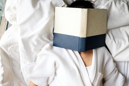 Woman reading a book with the face covered by the book.Morning with a book. Relaxing concept. Retro filter effect,soft focus,selective focus.

の写真素材