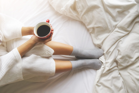 Beautiful asian woman hand holding a cup of coffee on the bed with morning light. Relaxing concept. Retro filter effect,soft focus,selective focus.の写真素材