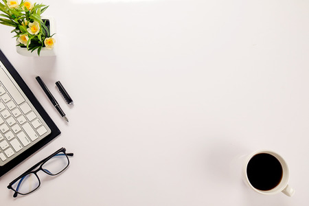 Office desk table with keyboard, notebook, pen, cup of coffee and flower. Top view with copy space (selective focus)の写真素材