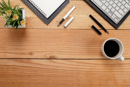 Office desk table with keyboard, notebook, pen, cup of coffee and flower. Top view with copy space (selective focus)の写真素材
