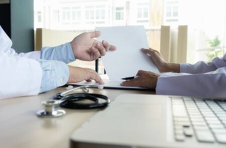 patient listening intently to a male doctor explaining patient symptoms or asking a question as they discuss paperwork together in a consultationの写真素材