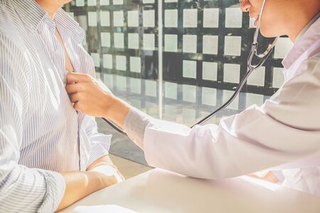 Doctor listening to cheerful young patients chest with stethoscope in his office at the hospital.の写真素材