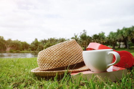 Book, cup of coffee,hat and earphone on the green grass. with woman feet.Morning with a book. Relaxing concept. Retro filter effect,soft focus,selective focus.の写真素材