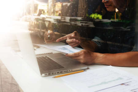 Asian business man manager analyzing datum in charts and typing on computer, making notes in documents on the table in office, vintage color, selective focus. Business concept.の写真素材