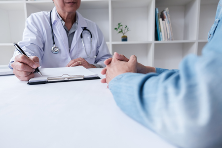 Patient listening intently to a male doctor explaining patient symptoms or asking a question as they discuss paperwork together in a consultationの写真素材