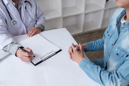 Patient listening intently to a male doctor explaining patient symptoms or asking a question as they discuss paperwork together in a consultationの写真素材