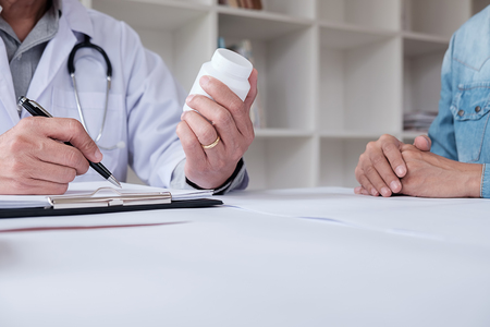 Patient listening intently to a male doctor explaining patient symptoms or asking a question as they discuss paperwork together in a consultationの写真素材