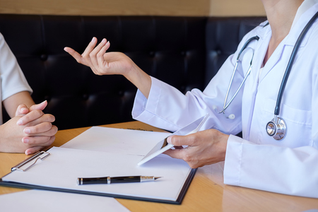 Patient listening intently to a male doctor explaining patient symptoms or asking a question as they discuss paperwork together in a consultationの写真素材