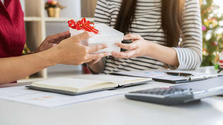 Business woman manager giving a present to her colleagues in last working day. Young creative people are celebrating holiday in modern office. Merry Christmas and Happy New Year.の写真素材