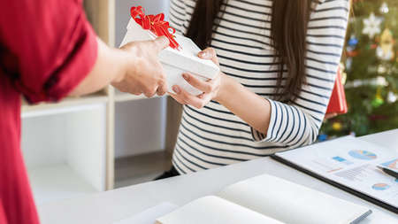 Business woman manager giving a present to her colleagues in last working day. Young creative people are celebrating holiday in modern office. Merry Christmas and Happy New Year.の写真素材