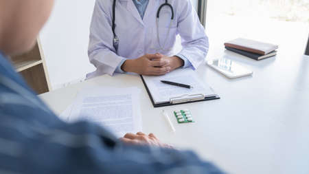 Patient listening intently to a male doctor explaining patient symptoms or asking a question as they discuss paperwork together in a consultationの写真素材