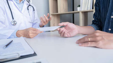 Patient listening intently to a male doctor explaining patient symptoms or asking a question as they discuss paperwork together in a consultationの写真素材