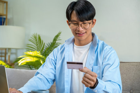 Young asian man holding credit card and using laptop computer at homeの写真素材