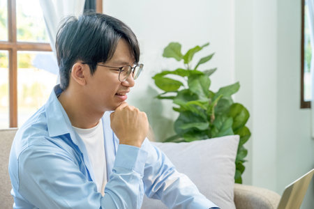 Asian man using laptop computer while sitting on sofa in living room at homeの写真素材