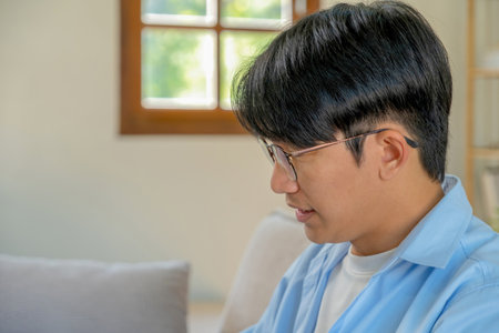 Portrait of Asian man sitting on sofa in living room at homeの写真素材