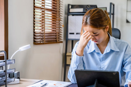 Businesswoman suffering from headache while using digital tablet at desk in officeの写真素材