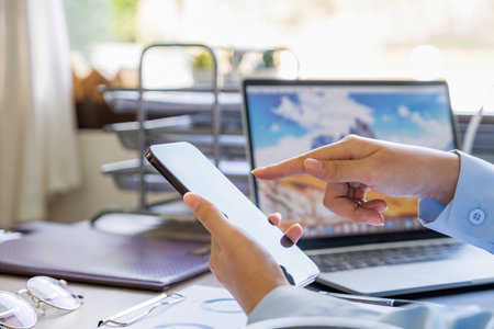 close up of businesswoman working with mobile phone and laptop in officeの写真素材