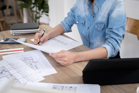 Cropped image of female architect working on blueprint at desk in office