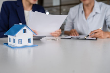 Real estate agent showing house model to customer at desk in office.の写真素材