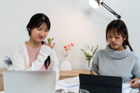 Female higher education student using laptop and studying book in home.の写真素材