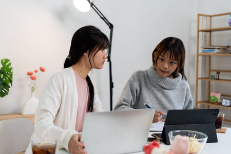 Female higher education student using laptop and studying book in home, Online learning.の写真素材