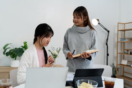 Female higher education student using laptop and studying book in home.の写真素材
