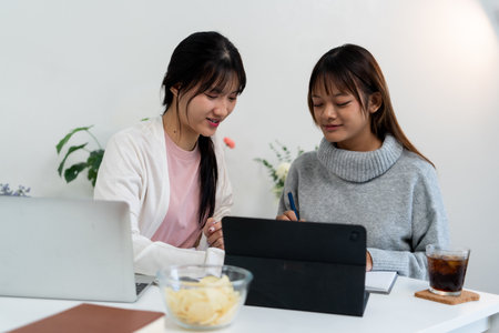 Female higher education student using laptop and studying book in home.の写真素材