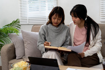 Female higher education student using laptop and studying book in home.の写真素材
