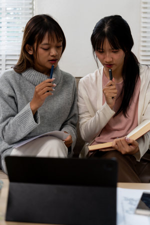 Two female higher education students using laptop and studying book at home.の写真素材
