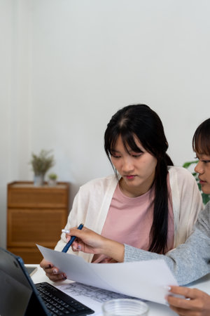 Two female higher education students using laptop and studying book in home.の写真素材