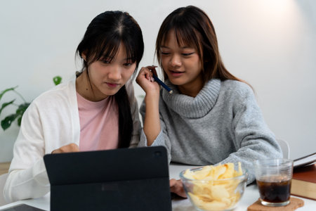 Female higher education student using laptop and studying book in home.の写真素材