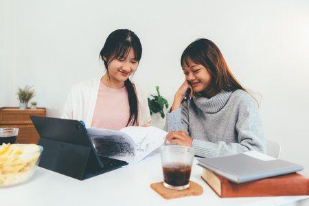 Two female higher education students using laptop and studying book in home.の写真素材