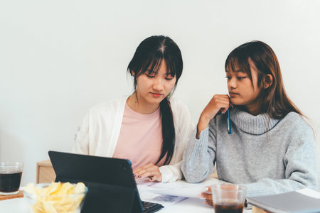 Female higher education student using laptop and studying book in home.の写真素材