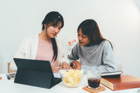 Female higher education student using laptop and studying book in home.の写真素材