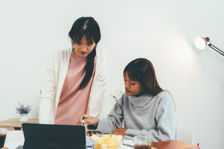 Two females using laptop and studying in home.