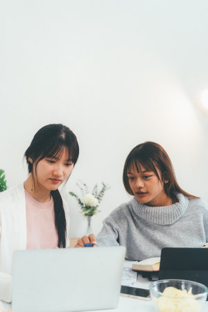 Female higher education student using laptop and studying book in home, Online learning.の写真素材