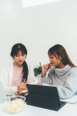 Female higher education student using laptop and studying book in home, Online learning.の写真素材