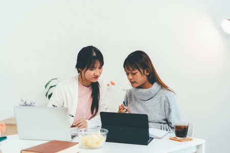 Female higher education student using laptop and studying book in home, Online learning.