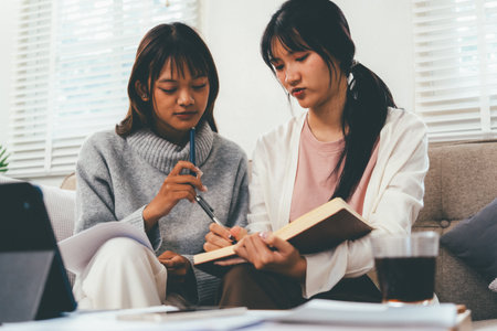 Female higher education student using laptop and studying book in home, Online learning.の写真素材