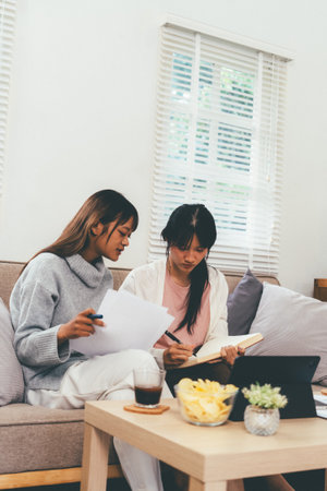 Female higher education student using laptop and studying book in home, Online learning.の写真素材