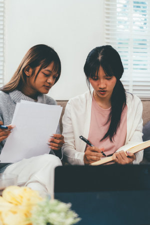 Female higher education student using laptop and studying book in home, Online learning.の写真素材