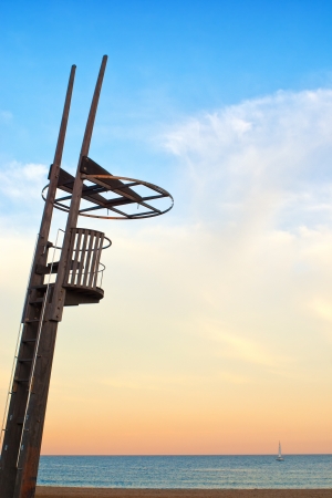 A wooden empty lifeguard seat overlooking a dusky sky with a small boat in the backgroundの写真素材