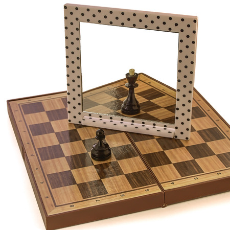 photo of a black pawn standing on a chessboard and dreaming of becoming a Queen with powerの写真素材