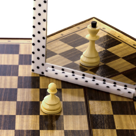 photo of a white pawn standing on a chessboard and dreaming of becoming a Queen with power,の写真素材