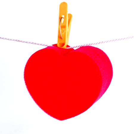 Red paper heart hanging on the yellow primako on the rope. Gray concrete background, horizontal...