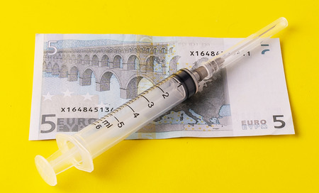 money for which to buy medical ampoules and a syringe, isolated on a yellow backgroundの写真素材