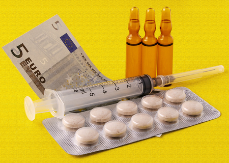 money for which to buy medical ampoules and a syringe, isolated on a yellow backgroundの写真素材