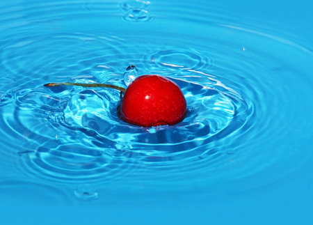 The ripe sweet cherry falls in blue water